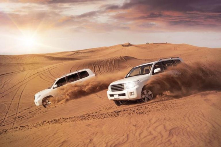 A photo of 4x4s driving across dunes in the desert.