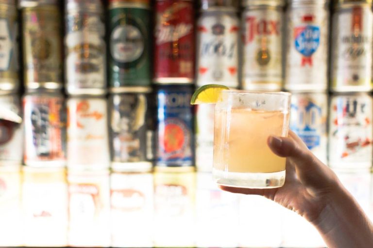 A photo of a person holding a glass in front of many cans.